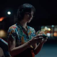 Foto da campanha de Burger King para o Whopper de Plantas. A foto apresenta uma mulher encostada em seu carro, durante a noite, prestes a comer o Whopper de Plantas.