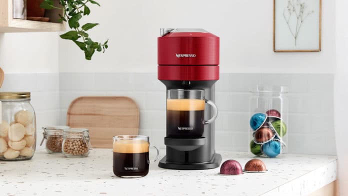 Nova máquina tecnológica da Nespresso. A foto apresenta uma mesa com a máquina, cápsulas, duas xícaras de café e doces pela mesa.