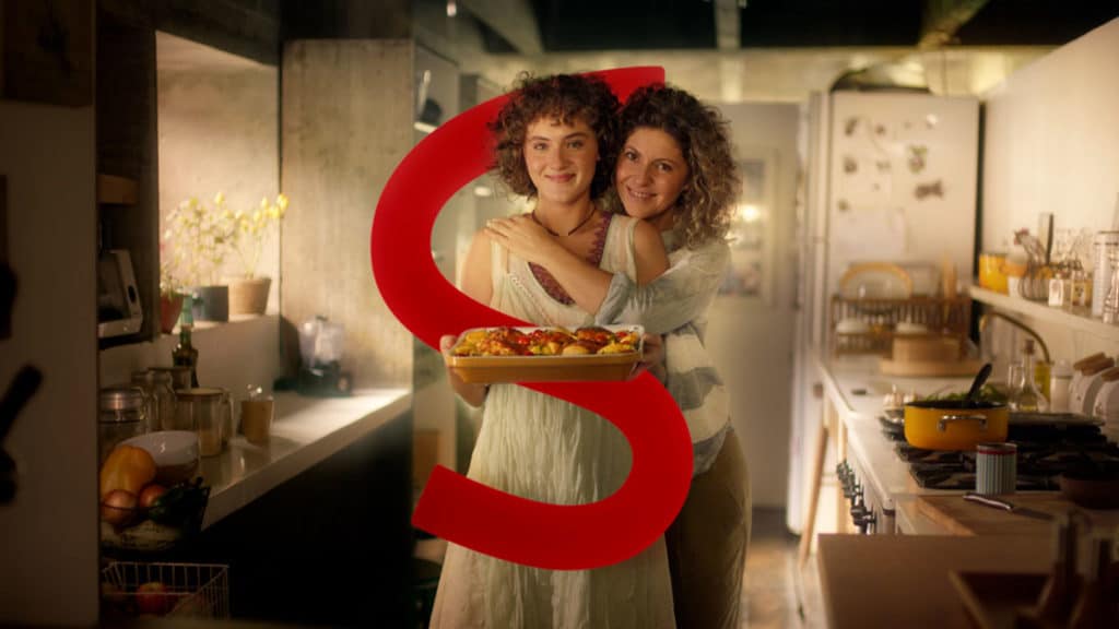 Foto de divulgação para a campanha interativa de dia das mães da Sadia. Na foto aparece uma mãe e filha abraçadas na cozinha, com a filha segurando um prato de frango e um grande "S" de Sadia dando uma volta nas duas.