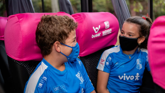 Foto de divulgação para o anúncio do patrocínio da Buser para o Tênis de Minas. A foto apresenta duas crianças com o uniforme da equipe sentadas dentro do ônibus da marca.