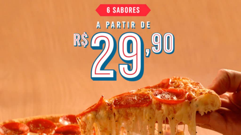 Foto de divulgação da promoção de pizza por R$ 29,90 da Domino's. A foto apresenta uma pessoa pegando um pegado de pizza de Pepperoni, e acima está escrito "6 sabores a partir de R$ 29,90".