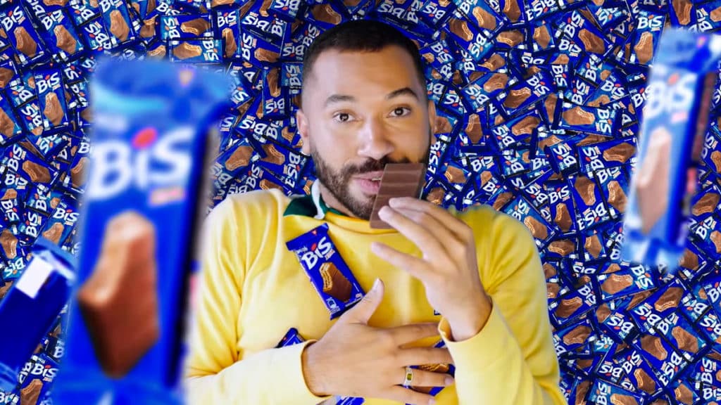 Nova campanha de Bis Xtra com Gil do Vigor. A foto apresenta o Gil deitado em meio a um monte de Bis Xtra, enquanto cai mais chocolate em cima dele e come um dos tabletes.