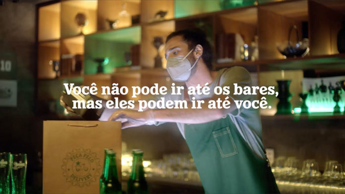 Campanha da Heineken para ajudar os bares na final da Champions League. A foto apresenta um homem empacotando cervejas no bar e com máscara, no meio da tela tem a frase 