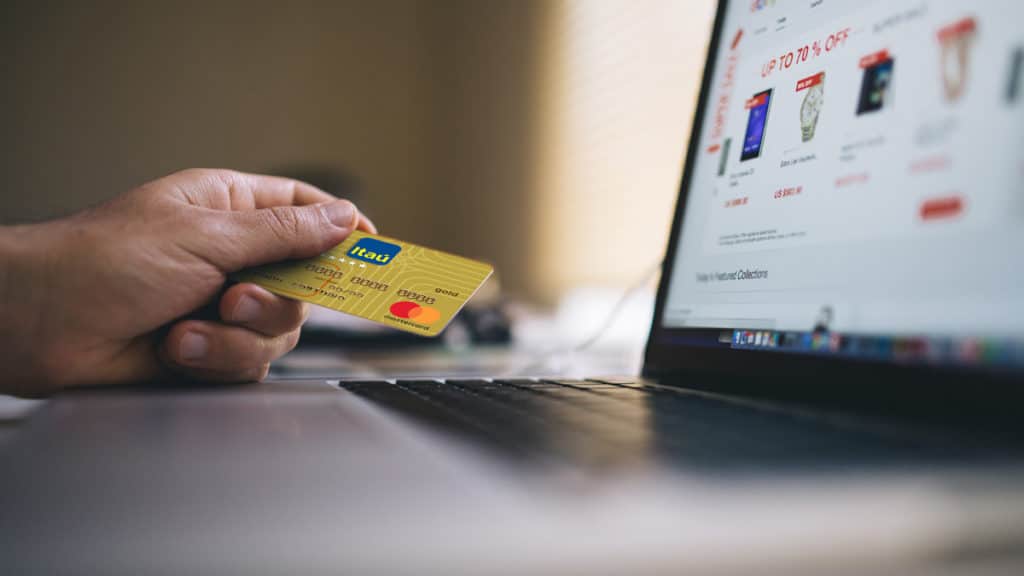 pesquisa-consumo-brasileiro-2021 A foto apresenta a pessoa segurando um cartão Itaú ao lado de um computador.