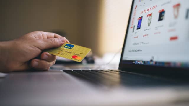 A foto apresenta a pessoa segurando um cartão Itaú ao lado de um computador.