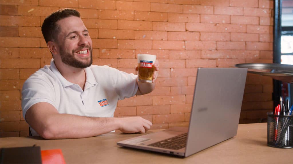 Foto de divulgação da ação em que Brahma procura um consumidor para tomar chopps de cerveja, a fotografia apresenta o humorista Maurício Meirelles tomando uma cerveja em frente ao notebook.