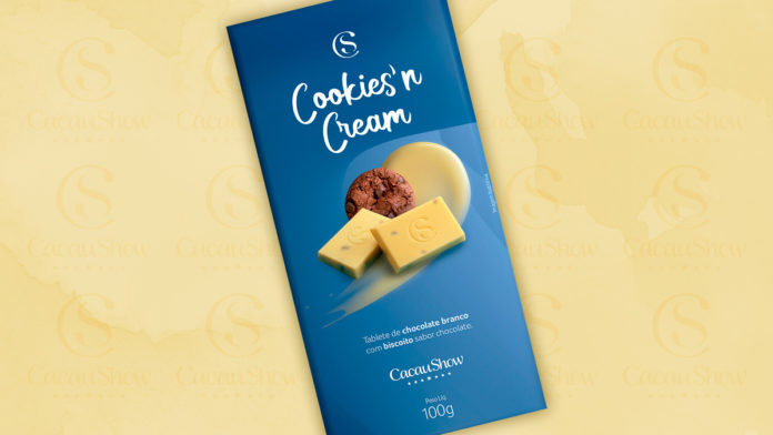 A foto apresenta a embalagem do Tablete Cookies'n Cream, uma das novidades de chocolate branco da Cacau Show, em um fundo na cor creme com o logo da marca.