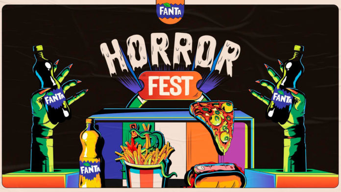 A foto apresenta o nome do evento Fanta Horror Fest, com vários elementos que remetem ao Halloween, como mãos de monstros e fundo preto, junto com uma TV, comidas e garrafas de Fanta espalhadas pela foto.