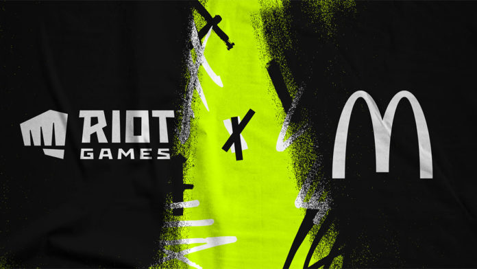 A foto apresenta o banner da parceria em League of Legends, em que é possível ver o logo da Riot e do McDonald's com um fundo preto e ver atrás.