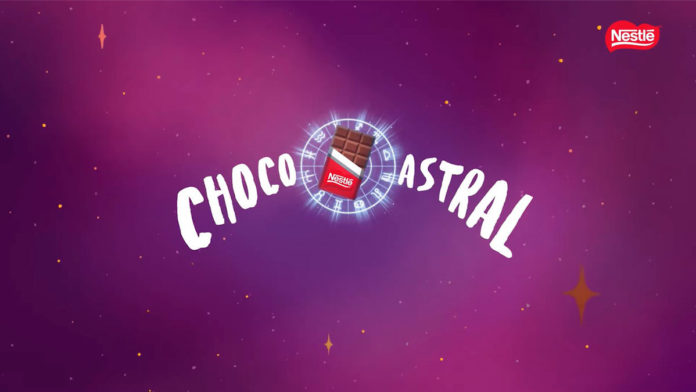 A foto apresenta um fundo roxo de universo com o nome ChocoAstral escrito no meio e uma barra de chocolate Nestlé, logo da promoção que irá selecionar os mapas astrais mais impactados negativamente.