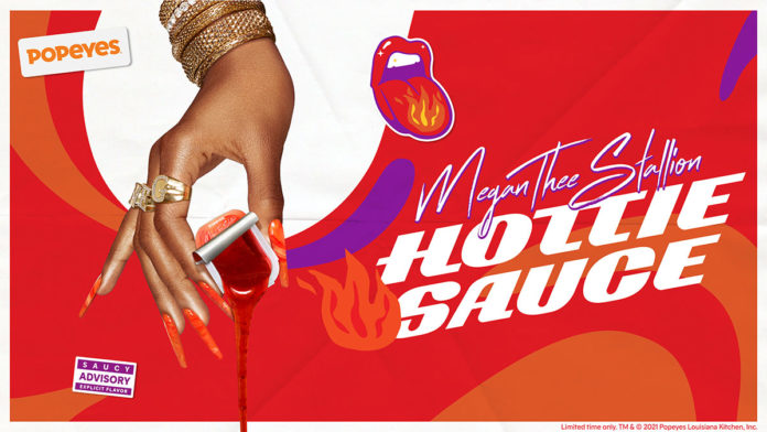 A foto apresenta a mão da Megan Thee Stallion derruabando o Hottie Sauce, ao lado do lago da collab e do Popeyes, com um fundo colorido com desenhos de fogo.