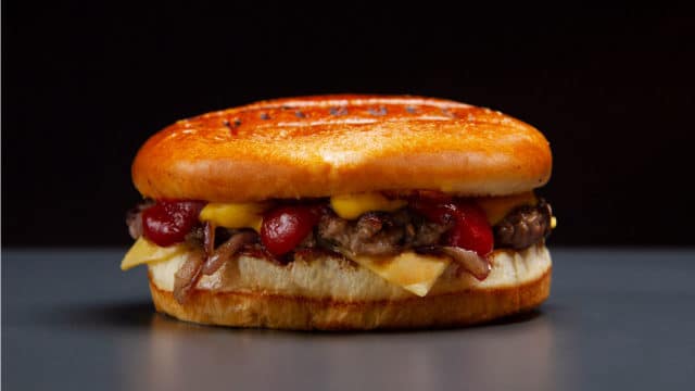 A foto apresenta o hambúrguer de Black Friday do Bullguer em cima de uma mesa cinza e um fundo preto.
