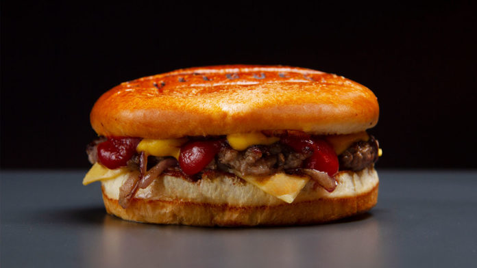 A foto apresenta o hambúrguer de Black Friday do Bullguer em cima de uma mesa cinza e um fundo preto.
