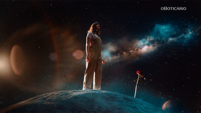A foto apresenta um frame do filme da campanha sobre memória olfativa de O Boticário, a imagem apresenta uma mulher em outro mundo olhando para o horizonte ao lado de uma rosa.