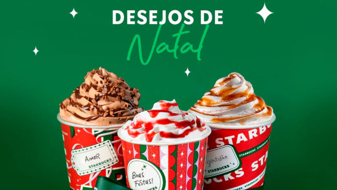 A foto apresenta as novas bebidas de Natal da Starbucks em um copo vermelho natalino e um fundo verde, junto a frase desejos de Natal.