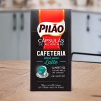 A foto apresenta a cápsula Pilão ideal para Latte em cima de uma mesa de madeira, em meio a uma cozinha.