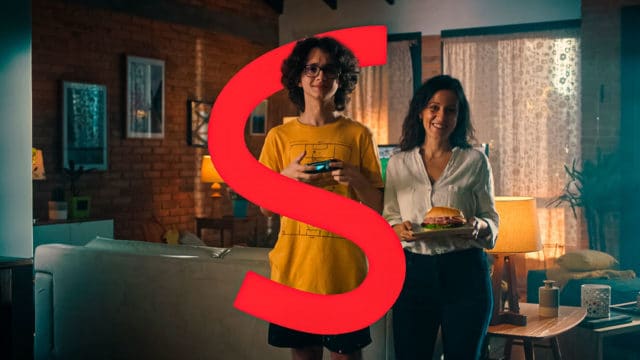 A foto apresenta a mãe e filho da campanha da Sadia segurando um controle de videogame e um lanche de presunto, respectivamente, com a letra "S" da marca dando uma volta no garoto.