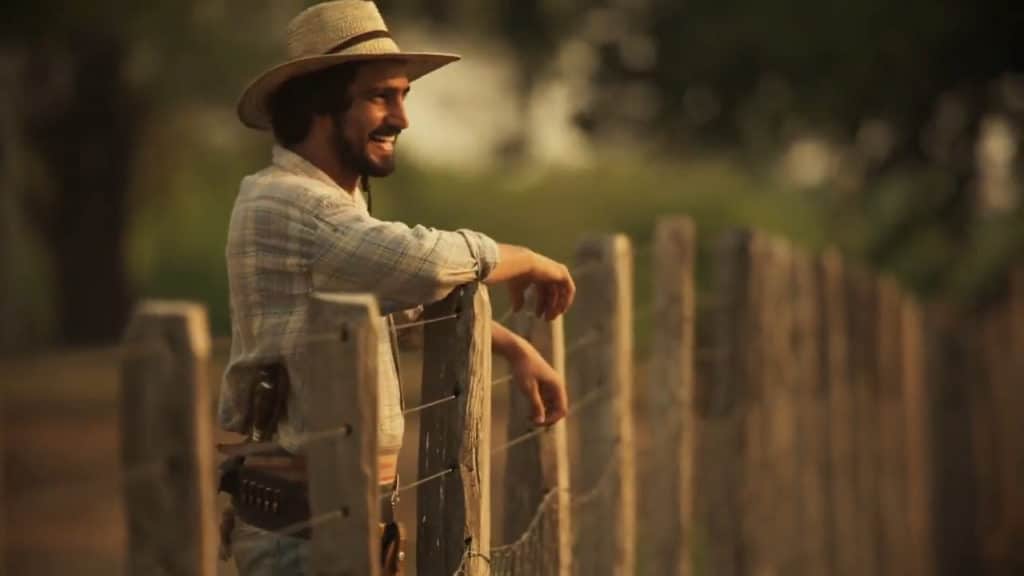 Personagem de Pantanal se apoia na cerca de uma fazenda