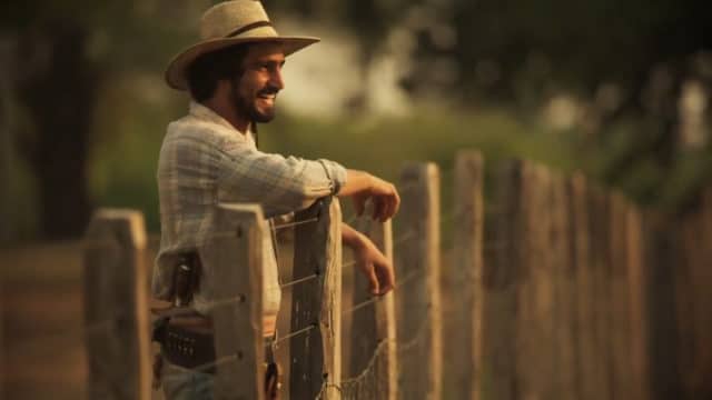 Personagem de Pantanal se apoia na cerca de uma fazenda