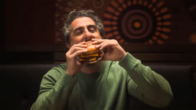 A imagem mostra o apresentador Marcos Mion mordendo um dos novos sanduíches do Outback