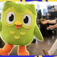 Na foto, Iberê Thenório, apresentador do canal Manual do Mundo, aparece "apontando" para uma pessoa com a fantasia da coruja verde, que é mascote do Duolingo