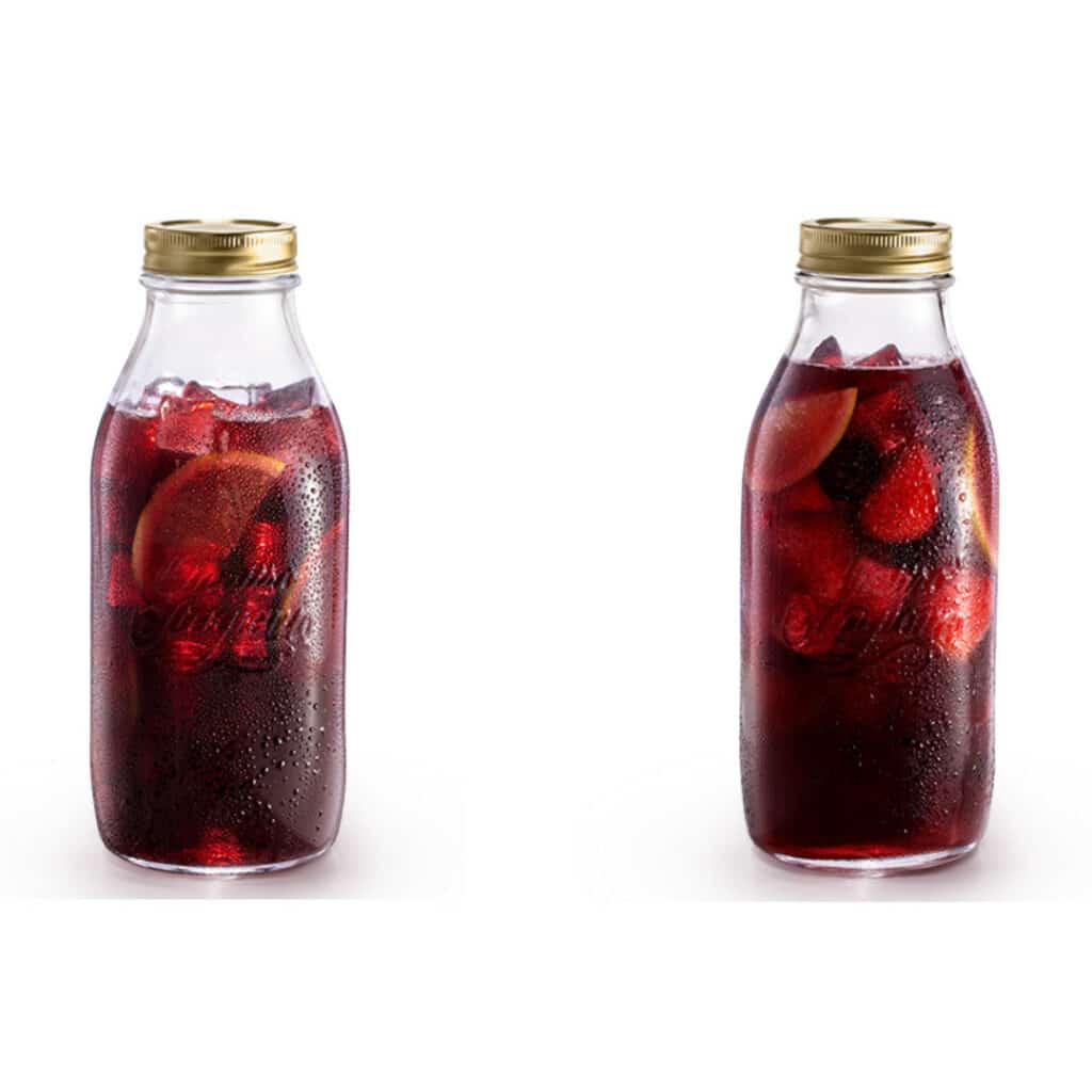Imagem mostra duas garrafas de vidro transparente contendo drinks preparados com vinho, gelo e fatias de laranja em seu interior.