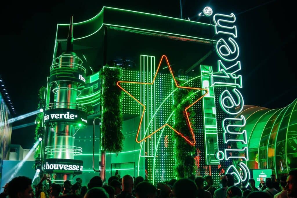 Celebração da Heineken com luzes verdes e decoração vibrante em um evento, com uma multidão reunida diante de um espaço festivo.