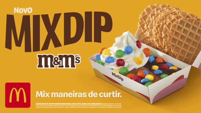 imagem com fundo amarelo traz embalagem de papel com sorvete, chocolate e confeitos coloridos. Na tampa da caixa de papel se vê alguns waffles. O texto traz os dizeres MixDip e M&M's.