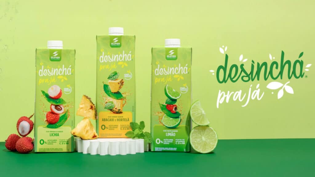 Imagem com o logo da linha "Desinchá Pra Já" juntamente com as embalagens dos sabores Chá Mate com Limão, Chá Verde com Abacaxi e Hortelã, e Chá Branco com Lichia