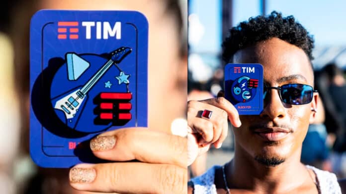 A imagem mostra duas pessoas segurando o TIM Block Pin, que será distribuído no Carnaval do RJ e Salvador, uma em close e outra mais distante.