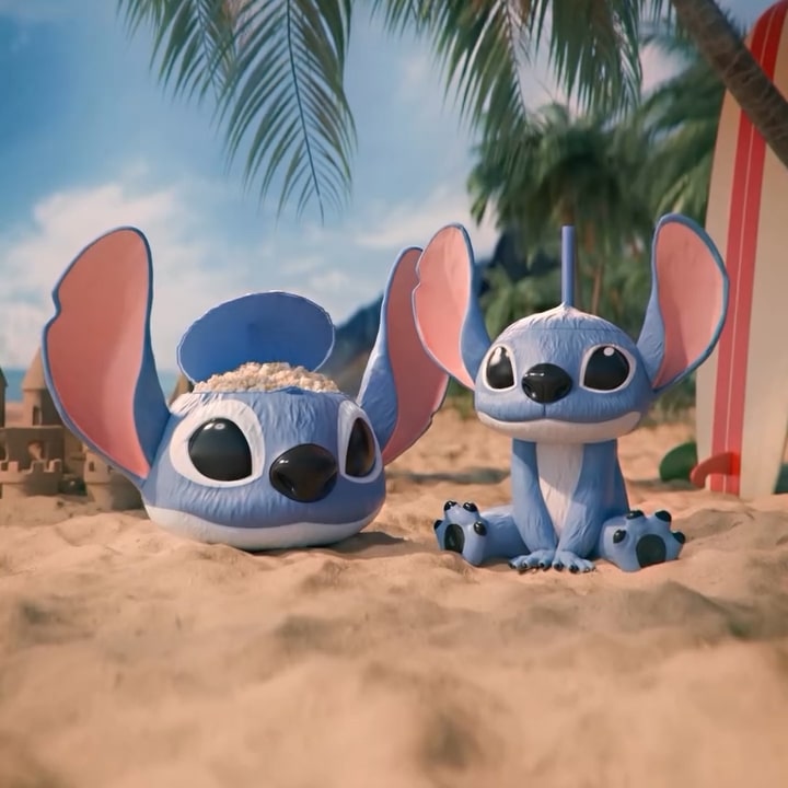 Duas versões do personagem Stitch em um ambiente de praia, uma como balde de pipoca com pipoca visível e a outra como um copo, ambos com cores vibrantes e detalhes característicos do personagem.