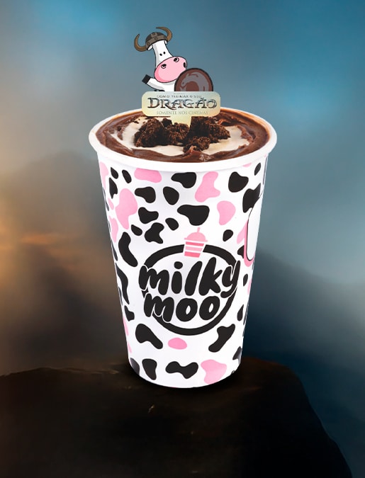 Copinho do milkshake 'Tempestade' da Milky Moo, decorado com granulado de chocolate e um topo de chocolate, contra um fundo de montanha e céu azul.