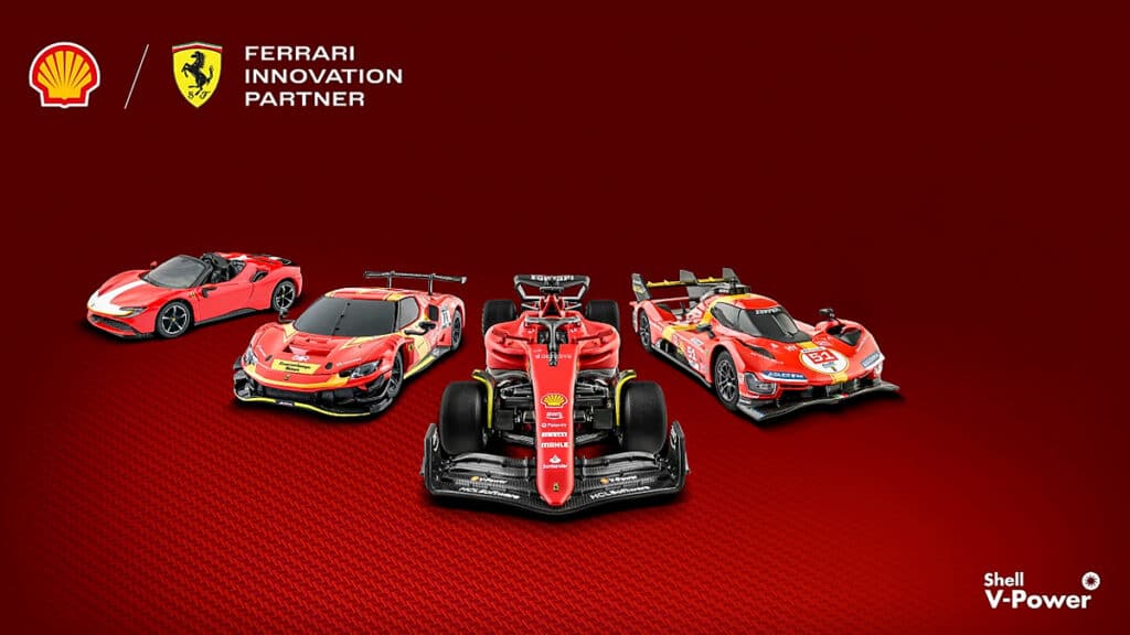 Imagem de quatro miniaturas de carros da Ferrari em um fundo vermelho, destacando a parceria com a Shell. Os modelos visíveis incluem um carro esportivo vermelho, um carro de corrida e outros dois veículos com design esportivo, todos com a marca Ferrari e o logotipo da Shell V-Power.
