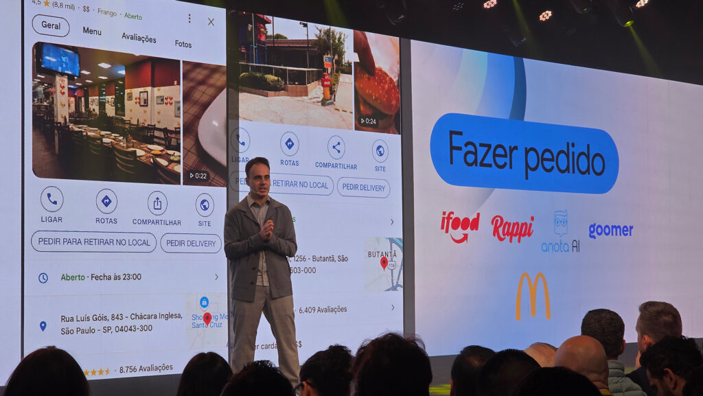 Um apresentador em um evento, em frente a telões exibindo informações sobre pedidos de delivery no Google Maps, com logos de serviços como iFood, Rappi e McDonald's visíveis.