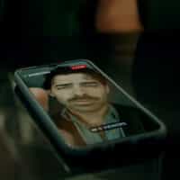 Celular sobre uma mesa exibindo uma live do cantor Joe Jonas no Instagram, com a indicação "LIVE" e o nome de usuário "@joejonas". A transmissão mostra Joe Jonas com expressão séria, bigode e cabelo ondulado. A live está com "0 viewers". Ao redor do celular, é possível ver parte da mão de uma pessoa com anel prateado e duas garrafas verdes da marca Heineken sobre porta-copos. A imagem sugere um ambiente de bar ou restaurante.
