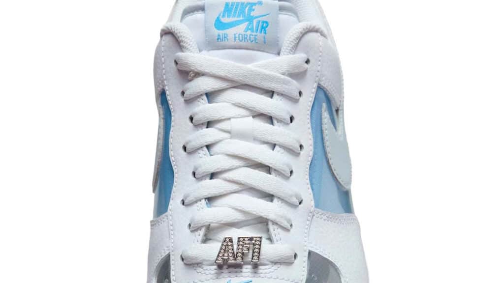 Modelo do tênis Nike Air Force 1 com parte superior em couro branco e detalhes em azul claro, incluindo a emblemática escrita 'AF1' em metal nos cadarços.