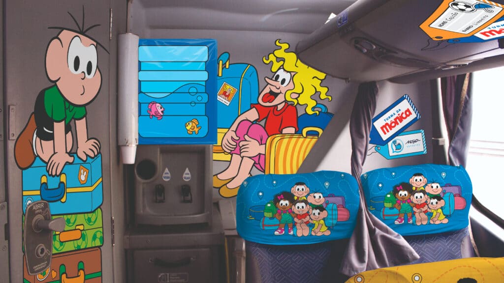 Interior de um ônibus temático da Turma da Mônica, com ilustrações dos personagens Mônica, Cebolinha e outros, decorando os assentos e as paredes.