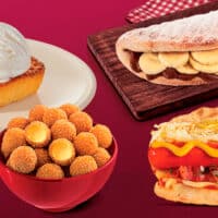 Prato com sobremesa de cocada de forno e sorvete de coco, bolinha de queijo crocante em um recipiente, sanduíche de hot dog com salsicha, purê e molho, e um pão doce recheado com banana e chocolate.