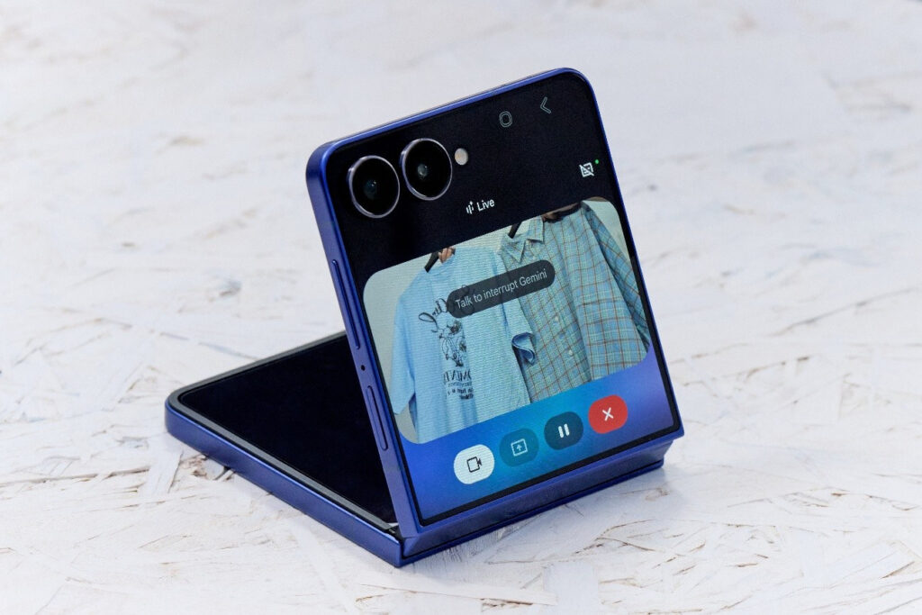 Smartphone Galaxy Z Flip7 em posição dobrada, mostrando a tela externa com uma interface interativa e câmera na parte traseira.