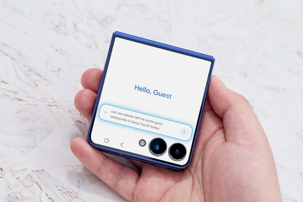 Mão segurando o Galaxy Z Flip7, exibindo a tela externa que mostra uma mensagem de boas-vindas e uma solicitação de pesquisa sobre restaurantes em Seul, Coreia do Sul.