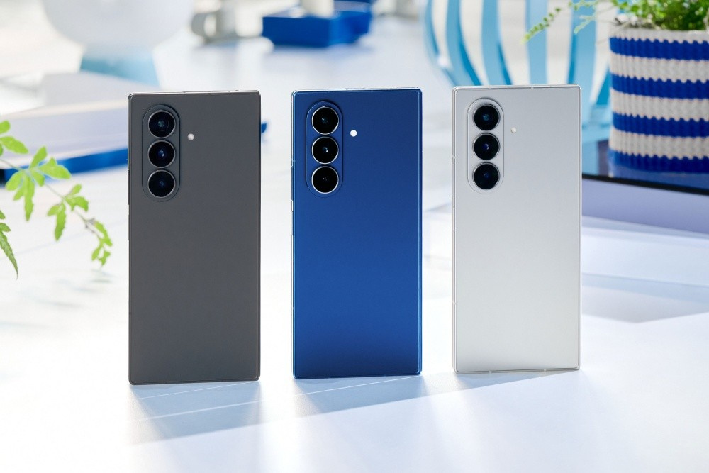 Três smartphones dobráveis Galaxy Z Fold7 e Galaxy Z Flip7 da Samsung, exibidos em pé sobre uma superfície clara, com cores distintas: um cinza escuro, um azul e um branco.