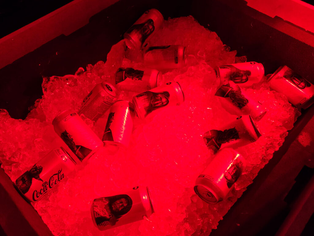 Latas de Coca-Cola com estampas de Star Wars repousam sobre gelo em um recipiente com iluminação vermelha.