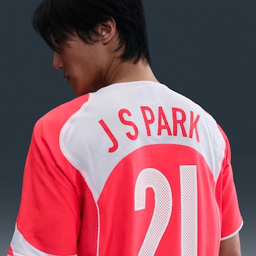 Um modelo de camiseta da seleção sul-coreana com o nome 'J SPARK' e o número 21, em uma combinação de cores rosa e branca.