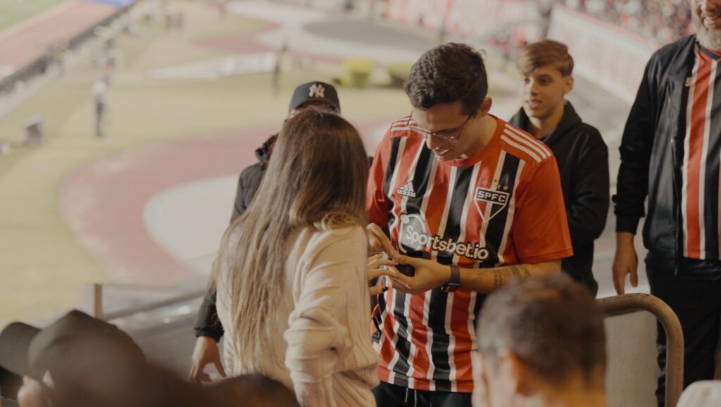 Casal durante um pedido de casamento no estádio Morumbi, com o noivo vestindo uma camisa do São Paulo e a noiva mostrando surpresa e felicidade.