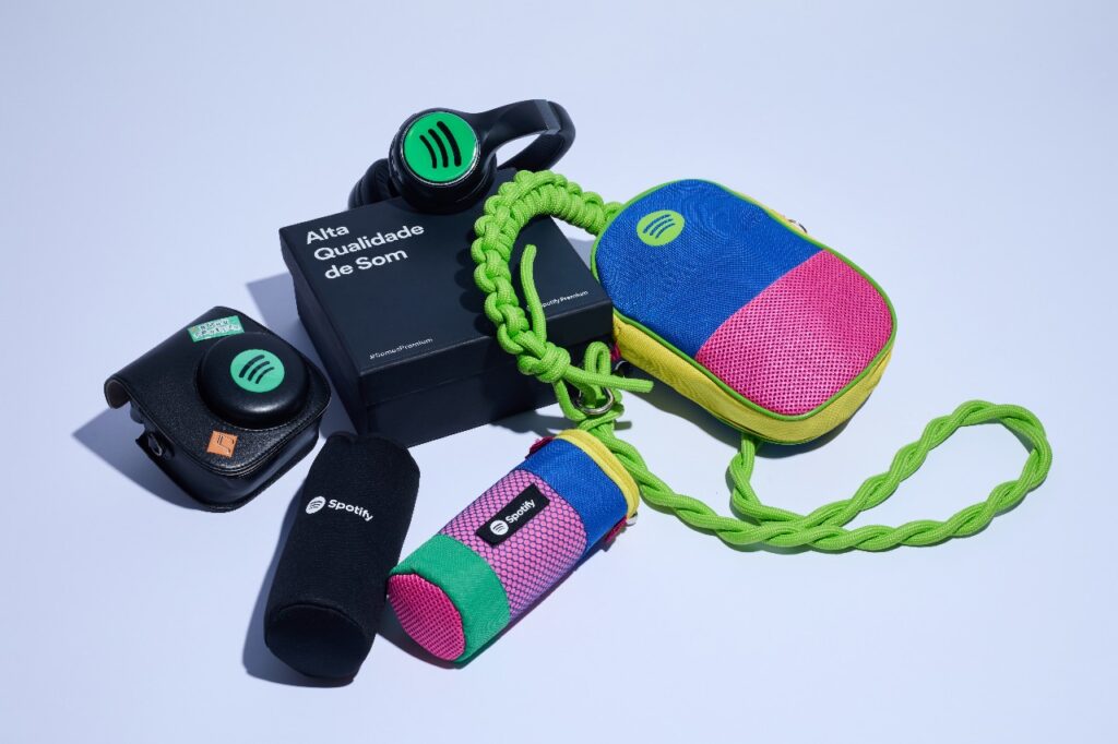 Kit promocional da Spotify com fones de ouvido, case para câmera, caixa JBL e bolsa personalizada, destacando design colorido e funcionalidade.
