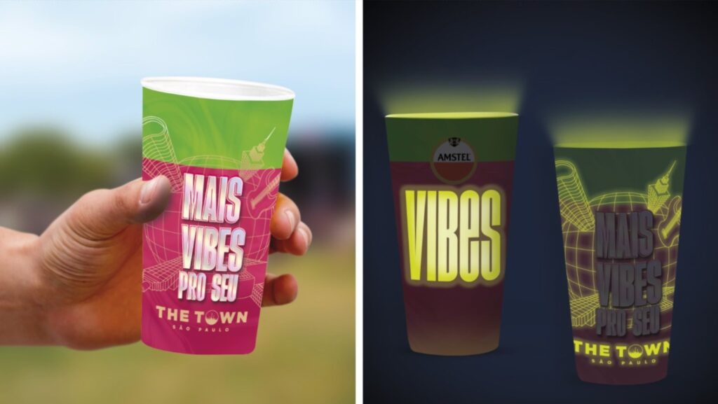 Copo que destaca a marca Amstel com os dizeres 'MAIS VIBES PRO SEU' e 'THE TOWN SÃO PAULO', segurado por uma mão, com cores vibrantes e design atraente, em um ambiente de festival.