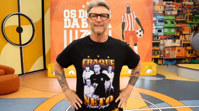 Craque Neto no set do programa "Os Donos da Bola" utilizando a camiseta escrito "Craque Neto Monstro Sagrado" juntamente com algumas fotos suas em montagem.