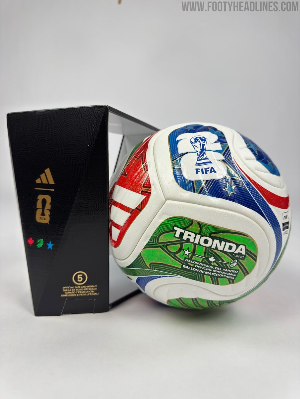 Bola de futebol Trionda, oficial da Copa do Mundo de 2026, com design em vermelho, azul, verde e branco, ao lado de sua embalagem da Adidas.