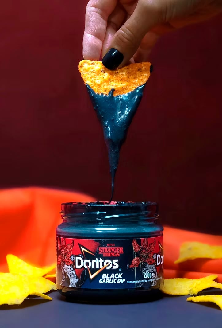 Um chip de Doritos mergulhado em um molho preto de alho, com uma embalagem temática de Stranger Things ao fundo.