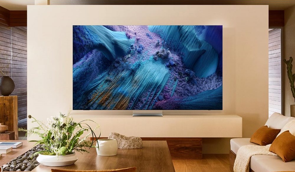 Imagem de uma TV moderna exibindo uma arte visual colorida, montada em uma parede clara dentro de uma sala de estar aconchegante, com móveis de madeira e plantas decorativas.